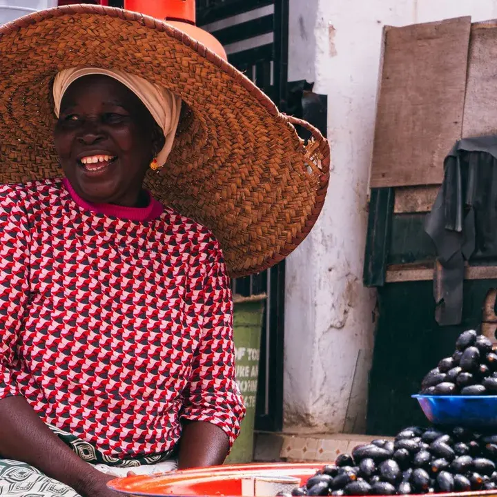An older trader in a wide straw hat, smiling.