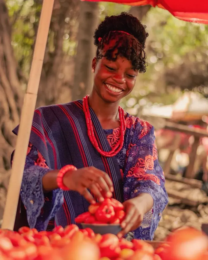 A trader laughing as she sorts tomatoes at her market stall.