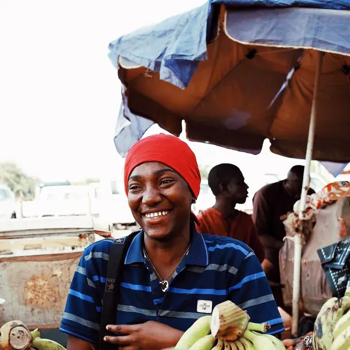 A young man in a red cap laughing at his banana stall.