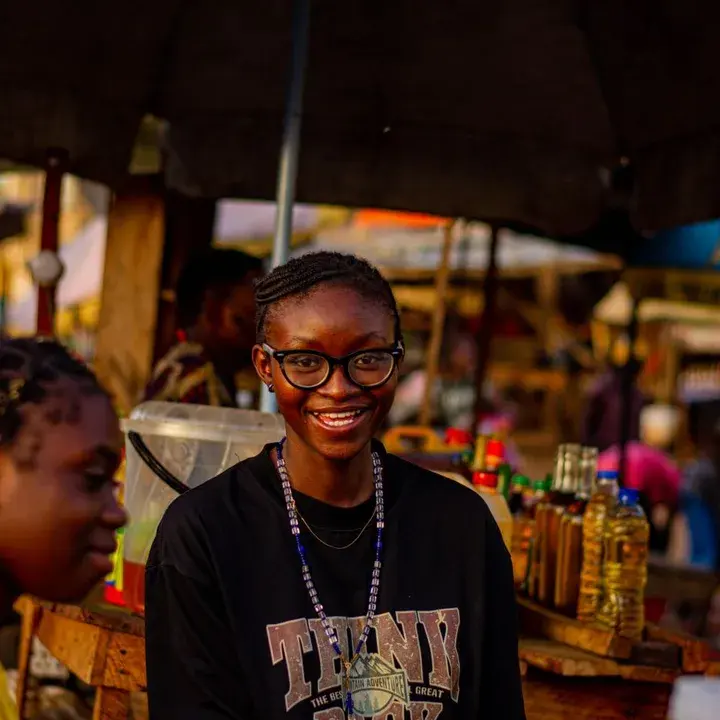 A young woman in glasses smiling in a busy market.